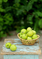 Homemade rustic green apples in a basket on an old stool.