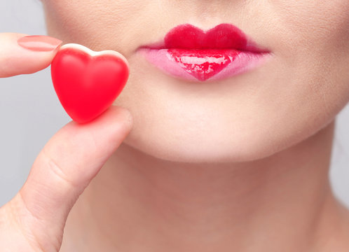 Woman holding tasty heart shaped jelly candy near her lips, closeup