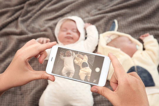 Mother taking photo of cute babies sleeping on bed