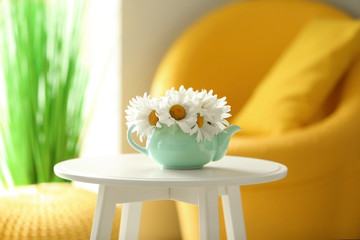 Teapot with chamomiles on white table in room