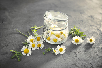 Fototapeta na wymiar Beautiful chamomiles and glass jar on grey background