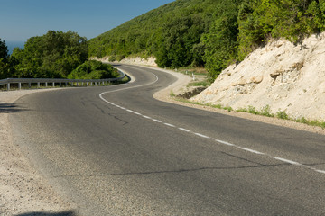 Naklejka premium Curvy paved road running away among rocky mountains with green trees.