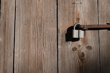 The new iron lock on an old metal fixing hangs on a high wooden gate
