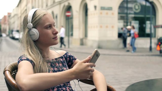 Young woman listen to music while sitting in cafe in the city, super slow motion
