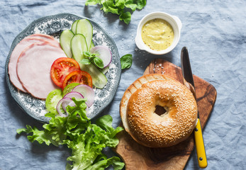 Bagel sandwich with ham, vegetables and green salad on a blue background, top view. Flat lay....