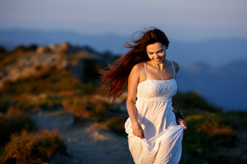 Beautiful woman in white dress running in the mountains. Jumping on mountain peak rock. Beautiful girl looking happy and smiling. Relaxing, feeling alive, breathing fresh air, got freedom from work