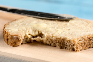 Flat lay butter spread on bread with knife and saltshaker served on a wooden board