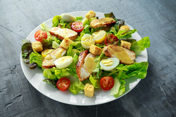 Fresh healthy Caesar salad with chicken, egg quail, tomatoes, Cheese and Croutons in a white plate