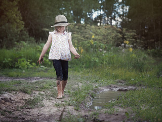 A child playing in a muddy puddle. Dirty girl in a hat and barefoot. Rural road