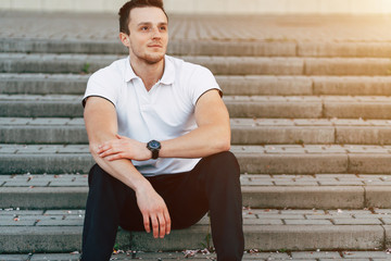 Obraz premium Portrait of Young Cheerful Muscular Man in White T-shirt Sitting on the Stairs