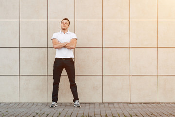 Fototapeta na wymiar Portrait of Young Muscular Man in White T-shirt Standing Near the Wall