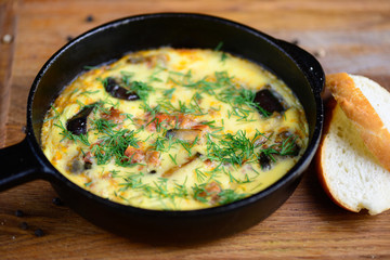 Omelet with vegetables, sprinkled with herbs, in a frying pan and two slices of bread on a wooden table. Closeup. Homemade dinner.