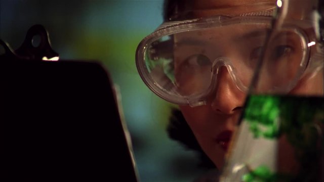 Female Asian scientist records data on clipboard.