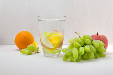 Detox water grape juice, apple, orange in a glass on white wooden background