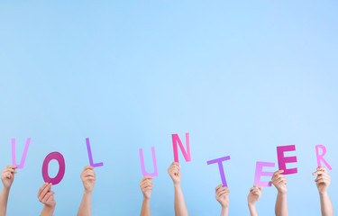 People putting hands in air together with word made of paper letters on light background. Volunteering concept