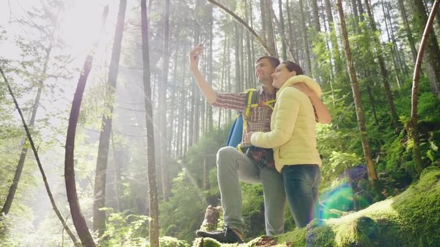 A couple in love of travelers with backpacks are photographed in the forest. The rays of the morning sun beautifully illuminate them