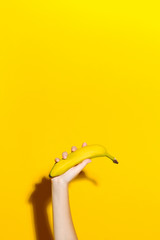 Female hand on a yellow background holds a fresh banana © alexbutko_com