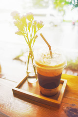 Close up a cup of take away iced Coffee with purple flower decoration and wooden plate at coffee cafe. wooden desk. filtered image with comic halftone vintage. light effect added.