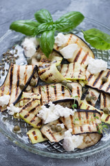 Close-up of grilled slices of aubergine and zucchini with cheese, capers and olive oil, vertical shot