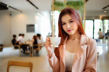 Portrait of beautiful woman holding a cup of coffee in her hand in blur background coffee shop, she drink coffee in the morning