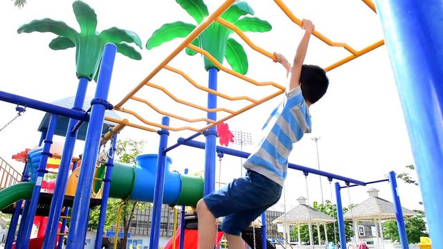 Slow motion of happy Young asian boy hang the yellow bar by his hand to exercise at out door playground under the strong sunlight in summer time.