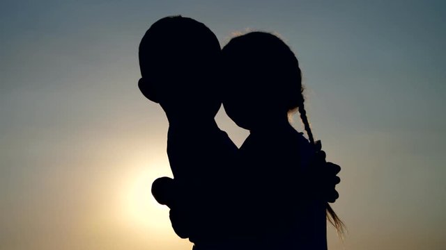 Silhouettes, figures of children, boy and girl, brother and sister hugging against the background of the sun, at sunset, in summer