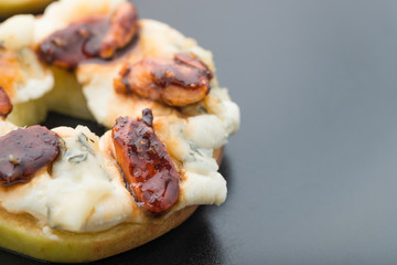 Apple circles with cream cheese, gorgonzola and spicy almond nuts with honey. Dark background
