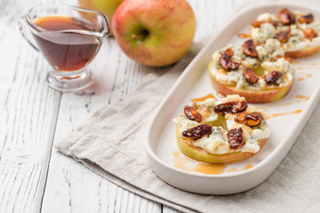 Apple circles with cream cheese, gorgonzola and spicy almond nuts with honey. Rustic white wooden table. Copy space