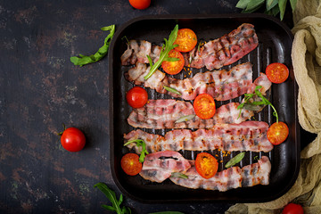 Fried bacon and tomatoes in pan on a dark background. Flat lay. Top view