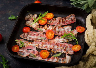 Fried bacon and tomatoes in pan on a dark background.