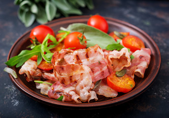 Fried bacon and tomatoes in plate on a dark background.