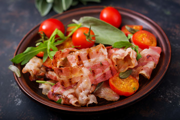 Fried bacon and tomatoes in plate on a dark background.