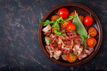 Fried bacon and tomatoes in plate on a dark background. Flat lay. Top view.