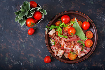 Fried bacon and tomatoes in plate on a dark background. Flat lay. Top view.