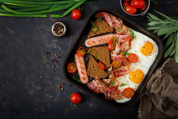 English breakfast - fried egg, sausage, tomatoes, bacon and toast. Top view. Flat lay