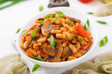 Stewed white beans with mushrooms and tomatoes with spicy sauce in a white bowl.