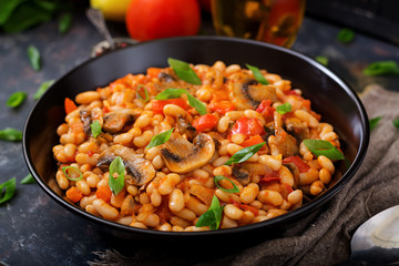 Stewed white beans with mushrooms and tomatoes with spicy sauce in a black bowl.