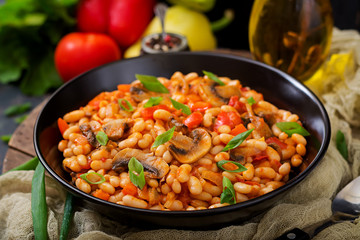 Stewed white beans with mushrooms and tomatoes with spicy sauce in a black bowl.