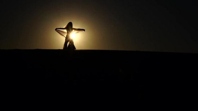 Girl performs beautiful belly dance on sunset background. Silhouette. Slow motion