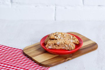Cantucci. Typical Italian cookies on a saucer of red color and on a white wooden background
