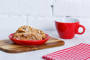 House biscuit of cantuccini or cantucci, the Italian cookies, on a saucer of red color with a cup of coffee on a white background