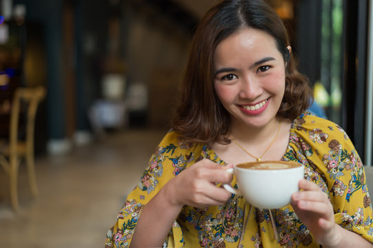 Portrait of beautiful woman and holding a cup of coffee in her hand in blur background coffee shop, she drink coffee in the morning