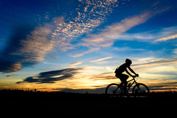 Naklejka na ściany i meble Silhouette of cyclist in motion on the background of beautiful sunset,ride bicycle on sunset background,Silhouette of man ride a bike in sunset background.