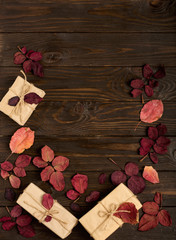 Flat lay frame of autumn crimson leaves and gift boxes on a dark wooden background.
