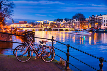 Fototapeta premium Skinny bridge and Amstel river in Amsterdam Netherlands at Dusk, selective foreground focus on bicycles