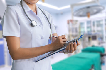 image of woman doctor in white coat report in a notebook on blur background of operating room, clipping path included