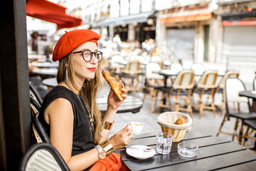 Young stylish woman in red beret having a french breakfast with coffee and croissant sitting...