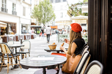 Fototapeta Young stylish woman in red beret having a french breakfast with coffee and croissant sitting oudoors at the cafe terrace obraz