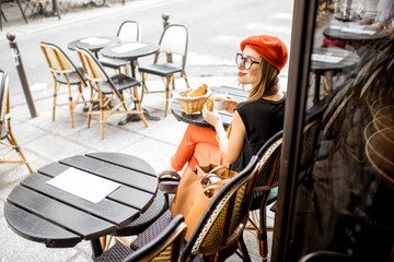 Young stylish woman in red beret having a french breakfast with coffee and croissant sitting...