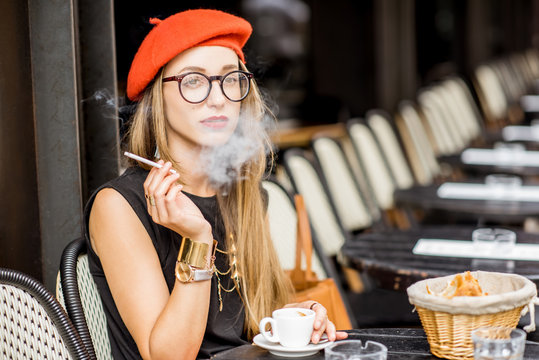 Portrait of a young stylish woman in red beret and eyeglasses smoking a cigarette